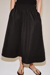 Falda midi de tiro medio color negro, con cintura elástica, bolsillos laterales ocultos y bajo con acabado en línea evasé.
