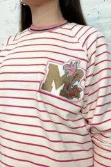 Buzo blanco a rayas horizontales rosas con cuello redondo a rayas rosas, marrones y blancas. Tiene un parche con la letra M dorada y una flor rosa.