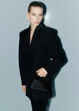 Bolso de mano tipo baguette, color negro, cubierto de pedrería brillante. Presenta un diseño estructurado con asa corta integrada y cierre superior.