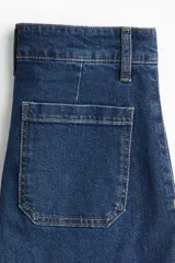 Jean de denim azul oscuro con tiro alto y corte wide leg de pierna ancha. Cuenta con bolsillos de parche delanteros y costuras pespunteadas a contratono.