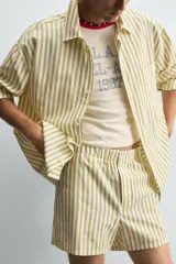 Shorts de hombre confeccionados en algodón con estampado de rayas verticales amarillas y blancas. Presenta cintura elástica, bolsillos frontales y un pequeño bordado de un pez en la parte inferior derecha.