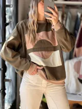 Buzo verde militar de calce relajado, confeccionado en friza de verano, con intervención artística artesanal en el frente mediante una composición abstracta de piezas textiles en tonos rosados, beige y marrón. Cuenta con cuello redondo, puños y dobladillo en rib elástico.