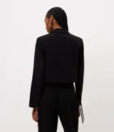 Blazer corto de sastre de la marca Cortelle, color negro, confeccionado en poliéster. Cuenta con cuello con solapa, mangas largas con amarre en los puños, bolsillos delanteros y cierre frontal por cordón ajustable con punteras metálicas.