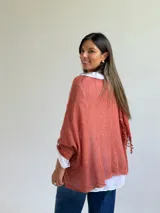Sweater de punto color naranja con diseño holgado, que incorpora franjas horizontales de encaje con motivos florales. Presenta mangas tres cuartos con puños abotonados y se complementa con una bufanda del mismo tejido y color.