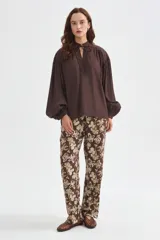 Blusa de lyocell color marrón, con diseño holgado, escote en V con cordón para atar y mangas largas abullonadas con puños ajustados.
