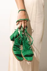 Sandalias de tacón estilo griego en gamuza verde, con tira acolchada en los dedos y tiras largas para atar alrededor de la pierna. Tienen un tacón de 4 cm.
