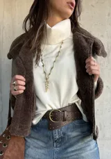 Campera tipo gamulán de cuero sintético en color vizón, con interior y solapas de piel sintética en color marrón oscuro. Presenta cierre frontal, correas ajustables con hebillas en los puños y diseño de corte recto.