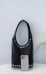 Cartera tipo hobo de cuero sintético color negro, con tachas plateadas en los bordes.