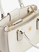 Cartera tote de poliuretano color blanco con acabado texturizado y motivo integral del monograma TH en bajo relieve. Cuenta con dos asas superiores, correa cruzada extraíble y detalles metálicos dorados, incluyendo el monograma TH en la parte delantera.