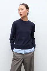 Sweater azul marino de manga larga con cuello redondo, combinado con una camisa celeste que se asoma por debajo.