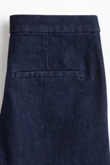 Jean de denim azul oscuro con tiro alto y corte acampanado, confeccionado con algodón elástico. Presenta bolsillos laterales al bies y cierre frontal oculto.
