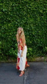 Vestido largo tipo solera con estampado floral de hibiscos en tonos naranjas y rojos sobre fondo blanco, con breteles finos y escote en V.