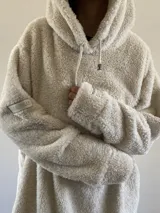 Hoodie oversize de textura tipo peluche, color beige, con capucha ajustable mediante cordones y ajuste en el ruedo inferior.