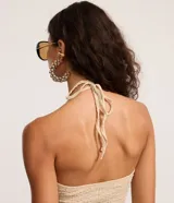 Blusa beige texturizada de corte halter con escote en V, lazo frontal ajustable en el busto y ruedo asimétrico ondulado.
