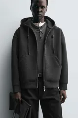 Sudadera con capucha de corte relajado confeccionada en tejido técnico con elasticidad y acabado efecto neopreno. Presenta cierre frontal de cremallera de doble dirección, bolsillos tipo canguro y terminaciones en rib.