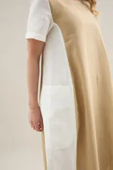 Vestido largo de lino de silueta relajada, con escote redondo, mangas cortas y bolsillos laterales. Cuenta con un diseño bicolor que combina un panel central en color tostado y los laterales y mangas en color blanco.