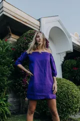 Vestido corto de lino color violeta, con escote off-shoulder y mangas tres cuartos con puños elásticos.