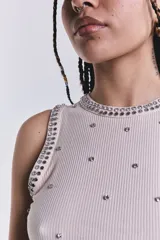 Musculosa beige de punto canalé con cuello redondo y sisa americana. Decorada con tachas y strass plateados.