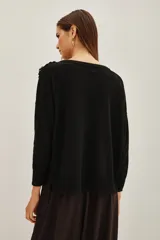 Sweater negro de punto con cuello redondo y mangas largas. Presenta una aplicación decorativa de lentejuelas y pedrería en tonos azules y oscuros sobre el hombro izquierdo.