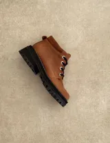 Borcego de cuero color gris con cordones color naranja, suela track negra de goma y detalle de gamuza en la parte superior del tobillo.