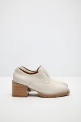 Zapato de cuero color beige, con taco de madera y suela dentada. Presenta un diseño slip-on con detalles de textura en relieve en los laterales y el empeine.