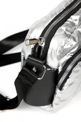 Cartera tipo bandolera de diseño acolchado en color plateado metalizado. Cuenta con dos compartimentos principales con cierre, detalles en negro y correa ajustable extraíble.