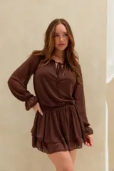 Vestido corto marrón de tejido semitransparente, con mangas largas abullonadas, escote redondo con cordones para ajustar y falda con volados en capas.