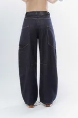 Jean de corte wide leg y tiro alto, confeccionado en denim de color azul oscuro. Presenta costuras decorativas visibles en los laterales y un diseño de pierna amplia.