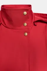Cazadora roja de cuello subido con capucha y manga larga, bolsillos delanteros y cierre frontal cruzado con botones a presión dorados.