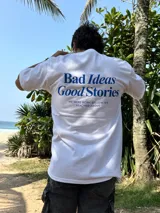Remera blanca de algodón con estampa azul en la espalda con la frase "Bad Ideas Good Stories".
