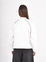 Buzo azul oscuro de corte holgado con cuello polo y escote en V. Presenta mangas largas con costuras raglán en color blanco y un estampado frontal con la palabra Ambience y el texto United Nation League en tonos dorados.