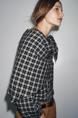 Camisa de manga larga con estampado a cuadros en blanco y negro. Presenta un cuello redondo y un pañuelo multiposición que cae en un drapeado asimétrico sobre el frente.