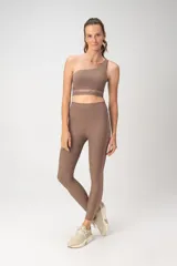 Top deportivo color beige, de un solo hombro, con banda inferior de mesh transparente.