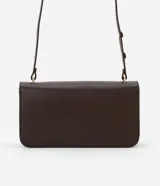 Cartera tipo shoulder bag de tamaño mediano, confeccionada en poliuretano color marrón oscuro. Presenta una solapa frontal con un detalle metálico dorado de forma orgánica y asa ajustable.