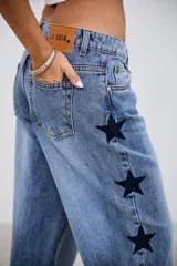 Pantalón de jean tiro medio con corte recto y holgado, presenta bordados de estrellas oscuras a lo largo de los laterales externos.