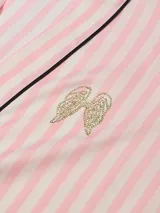 Bata de satén con diseño de rayas verticales en tonos rosados y blancos, con ribetes negros y detalle de bordado brillante en el pecho. Cuenta con mangas tres cuartos, bolsillos laterales y lazo ajustable en la cintura.