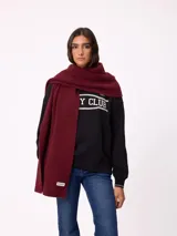 Bufanda de tejido de punto color bordó, larga y envolvente, con pequeña etiqueta de la marca en el extremo.