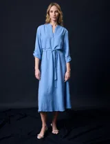 Vestido maxi color beige, con cuello mao y escote en V. Presenta mangas largas con presilla y botón para regular el largo, y un lazo ajustable en la cintura que marca la silueta.