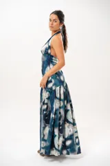 Vestido largo con escote halter profundo y diseño sin mangas. Presenta un estampado difuminado en tonos azules, celestes, blancos y grises, con corte ajustado en el torso y una falda larga con vuelo.
