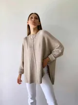 Buzo de tejido de punto color visón, con diseño holgado, cuello redondo, mangas largas con puños acanalados y costura central vertical visible. Presenta un ruedo asimétrico con aberturas laterales.