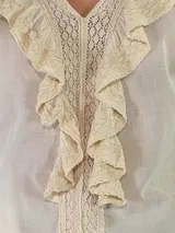 Blusa de algodón blanca con escote en V, mangas largas amplias y detalles de volados con encaje bordado en el frente.