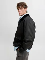 Campera de estilo worker en color negro, con acabado recubierto, cuello camisero en contraste, cierre frontal y bolsillos con solapa y broches a presión.
