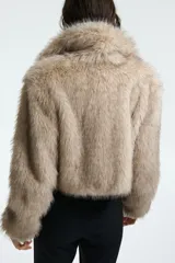 Campera corta de piel sintética en color beige, con cuello redondo, mangas largas y cierre frontal oculto.