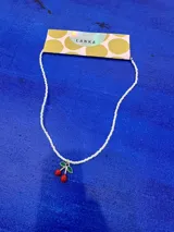 Collar corto tipo choker compuesto por pequeñas cuentas nacaradas blancas, con un dije central en forma de cerezas con hojas verdes esmaltadas.