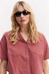 Camisa de manga corta color rosado, con cuello camisero, bolsillos frontales con solapa, botones a tono y diseño ligeramente recortado.