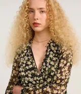 Vestido corto de chiffon negro con estampado de flores blancas y amarillas, escote en V, mangas largas abullonadas y volados en el busto.