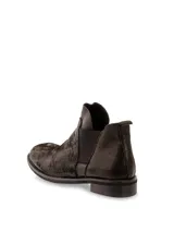 Botas Chelsea cortas de cuero negro, con elástico lateral y textura arrugada o plisada en la parte delantera. Poseen un taco bajo y bajo de goma.