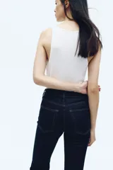 Jean de tiro alto con corte acampanado desde la rodilla, confeccionado en denim oscuro con cinco bolsillos y cierre frontal con botón.