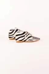 Botines acordonados con estampado de cebra en blanco y negro, puntera cubierta de glitter multicolor y suela plana color madera.