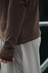 Remera deportiva marrón con cuello alto, cierre frontal parcial y mangas largas raglán, confeccionada en tejido técnico con paneles texturizados y corte ajustado.